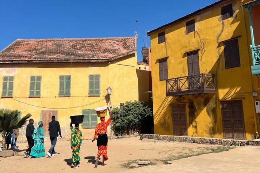 A group of people in traditional attire walking in front of a yellow building with a tiled roof. 3