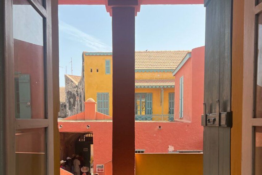 A view through an open door of a building with a red exterior and a yellow building in the background. 4
