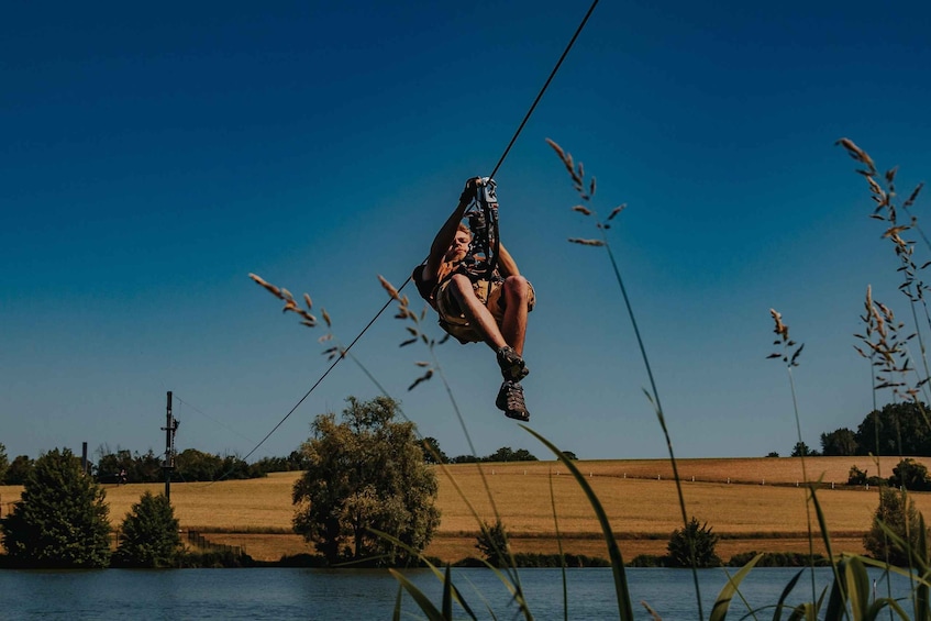 En person svæver på en zipline over vand med et landligt landskab i baggrunden. 4