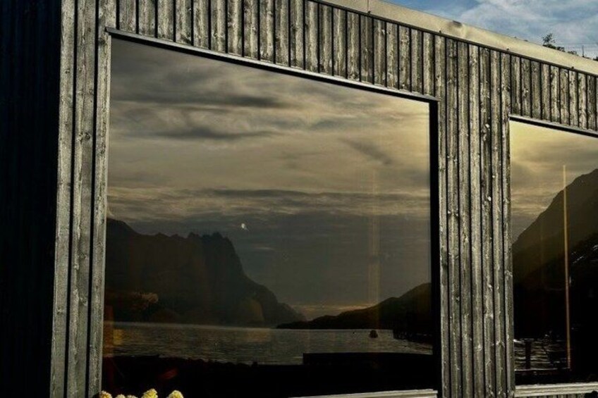 A wooden structure with large windows reflecting a mountainous landscape and a body of water. 5