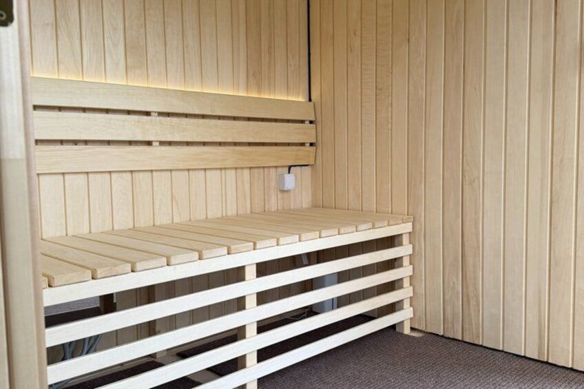 A wooden sauna bench with slatted design, a wall-mounted heater, and a power outlet. 4