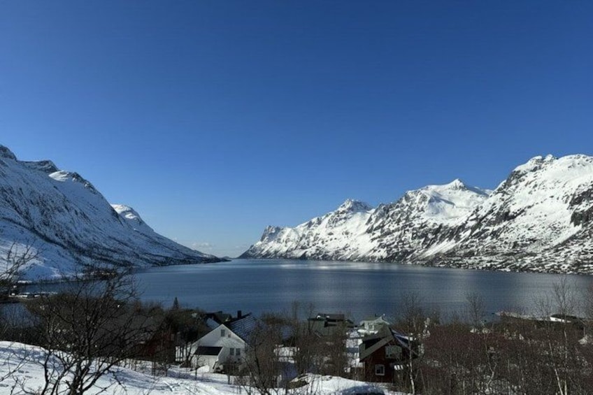 A snow-covered lake surrounded by mountains, a small house, and a clear blue sky. 3