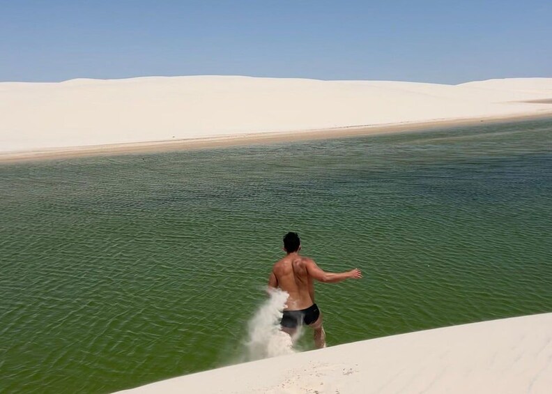A man in swim trunks standing in a body of water with sand dunes in the background. 4