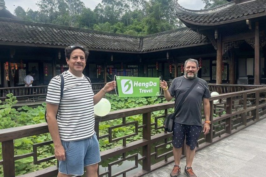 Two people standing in front of a traditional building with a green sign that reads 'HengDa Travel.' 2