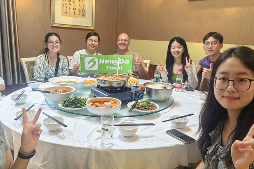 A group of people sitting around a table with various dishes, a bottle of water, and a smartphone on the table. 3