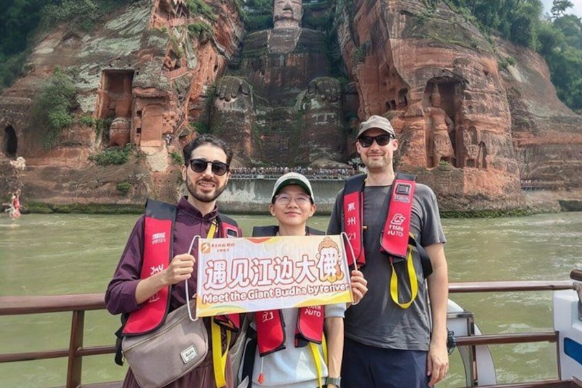 Three people on a boat with a sign in front of a rock formation with carvings. 1