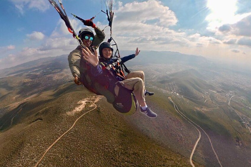 Two people paragliding over a mountainous landscape with winding roads below. 2