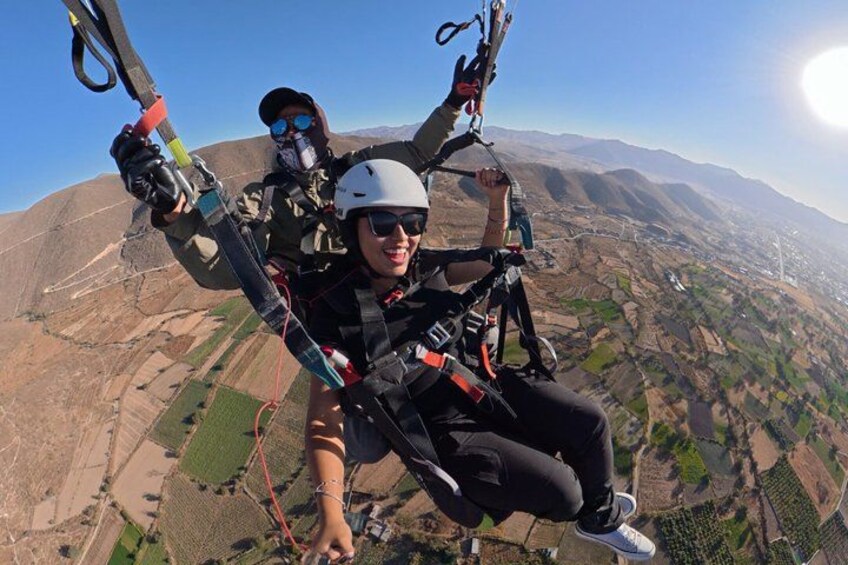 Two people skydiving with parachutes, high above a landscape with fields and mountains. 1