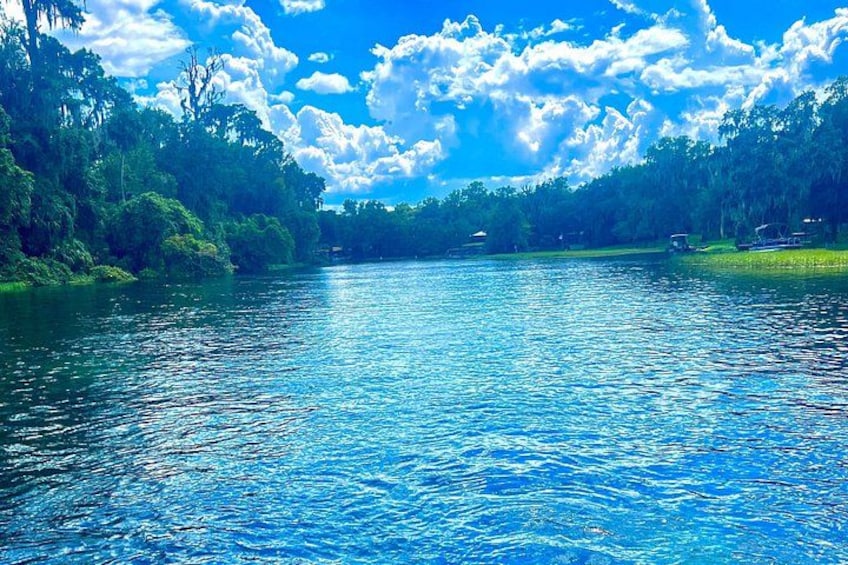 A calm river surrounded by lush greenery and a partly cloudy sky. 4
