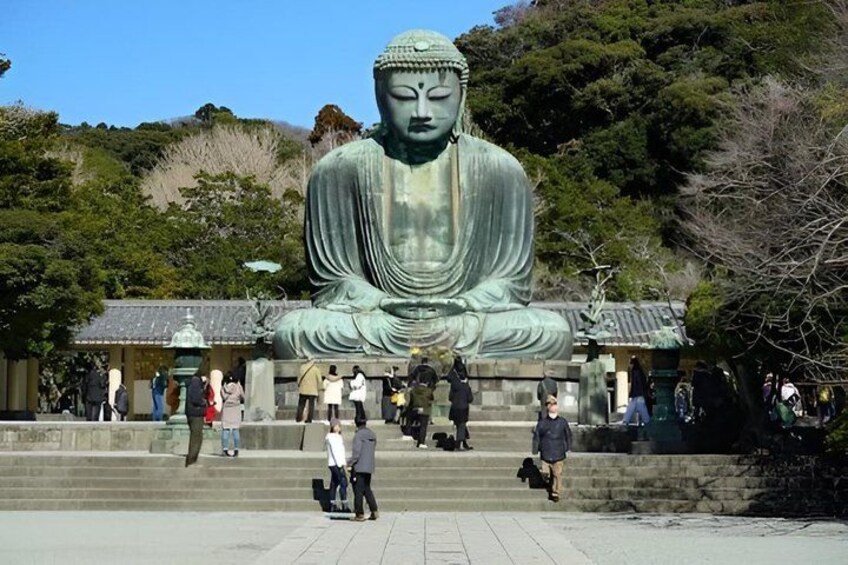 A large seated Buddha statue in a temple setting with visitors around. 4