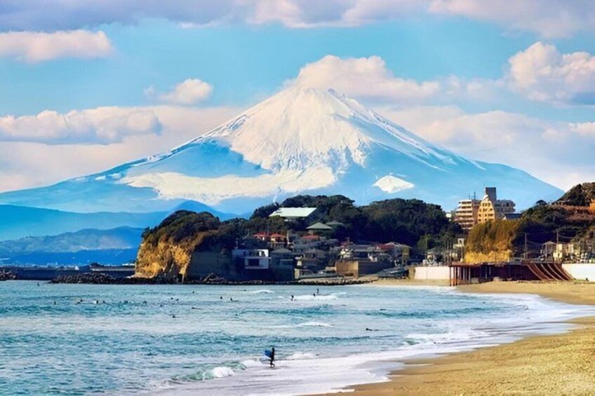 A beach with waves, a coastal town, and a snow-capped mountain in the background. 5