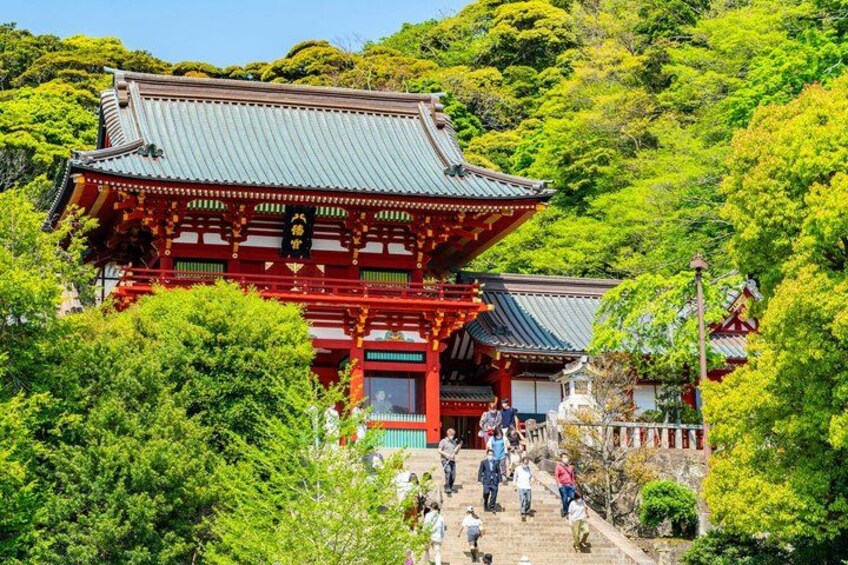A traditional Japanese building with a red roof and wooden structure, surrounded by lush greenery and a staircase leading up to it. 1