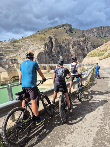 Un grupo de ciclistas sobre un puente, con un paisaje montañoso de fondo. 3