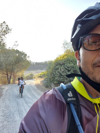 Un ciclista con casco y camiseta con logotipo visible pedalea sobre un camino de tierra, con otro ciclista al fondo. 4