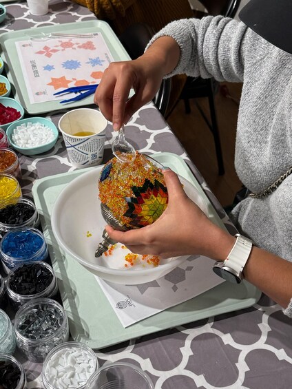 A person holding a colorful mosaic bowl, surrounded by various colored glass pieces on a table. 5