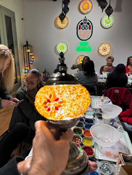 A group of people engaged in a craft activity, with a focus on a hand holding a beaded lamp. 2