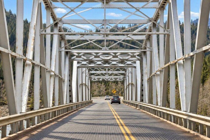 A metal bridge with a yellow centerline, surrounded by forested hills. 4