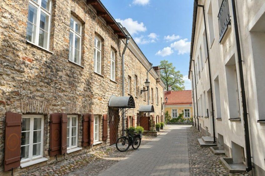 A cobblestone street lined with historic stone buildings, a bicycle parked in front of one building, and a clear blue sky. 5
