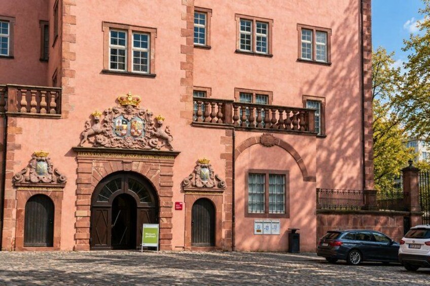 A pink brick building with ornate decorations, a balcony, and a signboard. 4