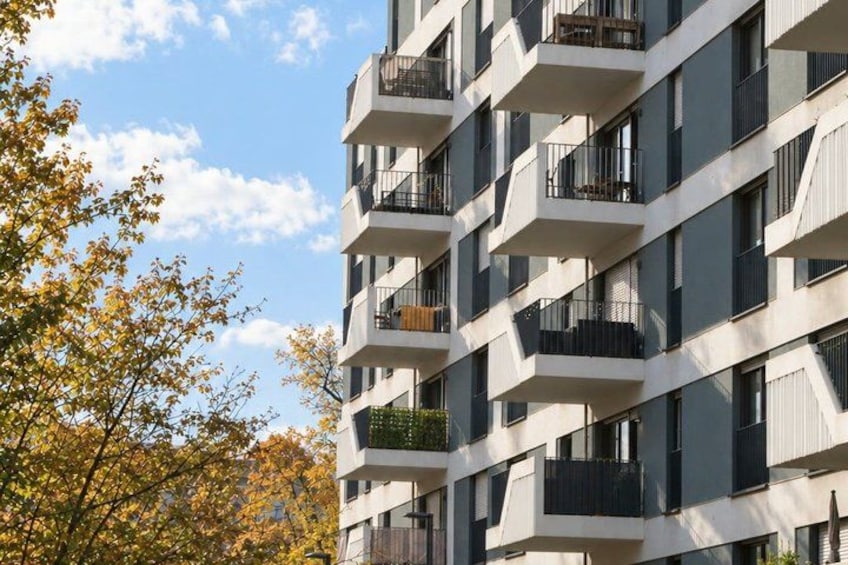 A multi-story building with balconies, surrounded by trees with autumn leaves. 2