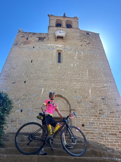 A cyclist with a bicycle in front of a historic stone tower. 5