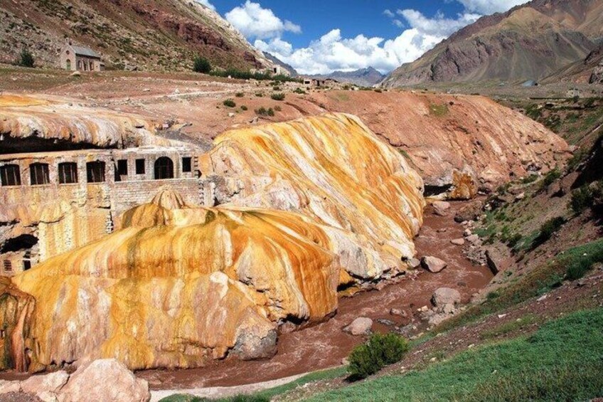 A river with sedimentary rock formations, a small building, and a mountainous landscape. 1