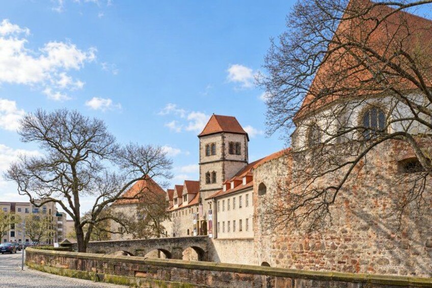 A historic stone building with a tower, a bridge, and leafless trees. 2