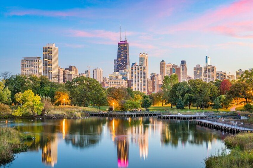 A city skyline with a prominent skyscraper, a calm lake reflecting the buildings, and a park with trees in the foreground. 2
