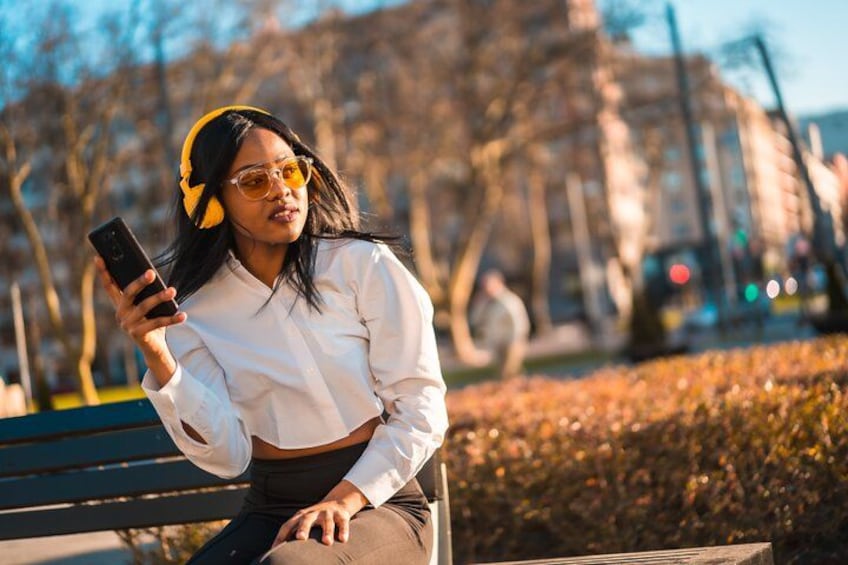 A person sitting on a bench in a park, holding a smartphone. 1