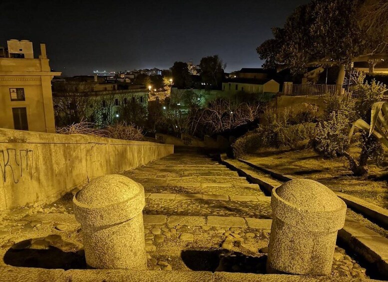 Vista nocturna de una escalera de piedra con separadores, rodeada de vegetación y edificios. 5