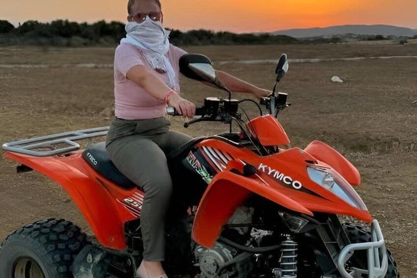 A person riding a red ATV in an open field with a sunset in the background. 2