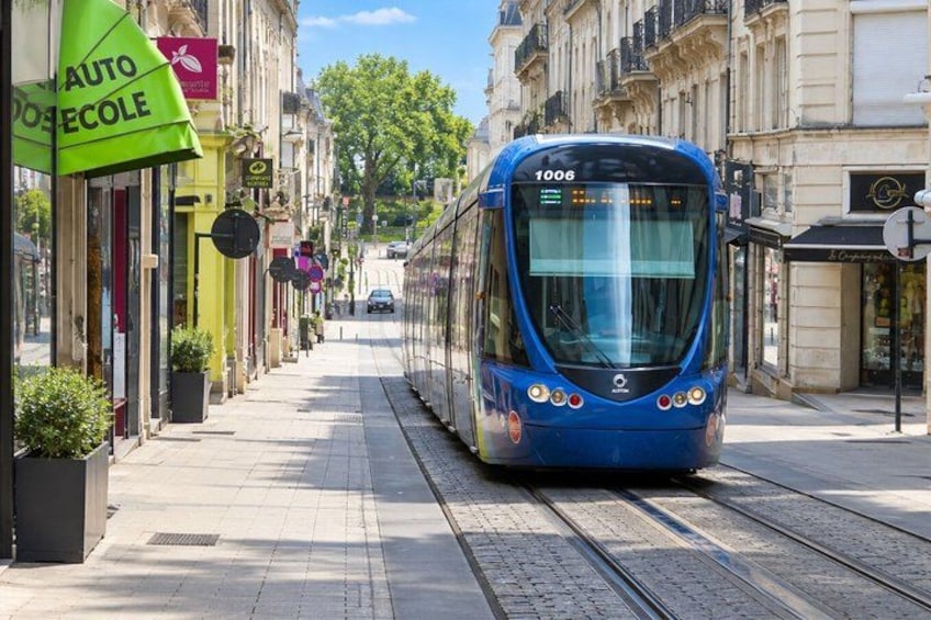A blue tram on a city street with buildings and shops on either side. 2