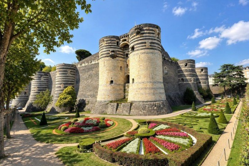 A historic castle with multiple round towers, manicured gardens, and a clear sky. 4