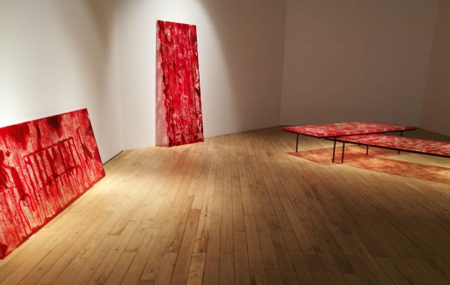 A room with wooden flooring, a red textured wall, and a red table. 2