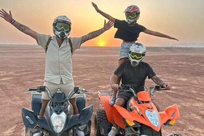 Two people on quad bikes with arms outstretched in a barren landscape at sunset. 1