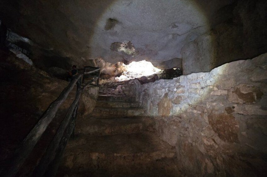 A dimly lit stone staircase in a cave with a wooden railing. 3