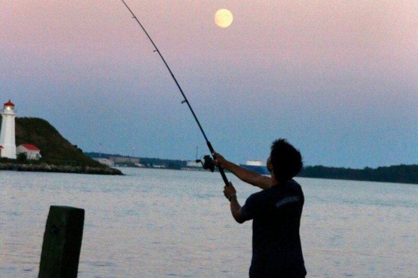 A person fishing by a lighthouse at dusk. 5