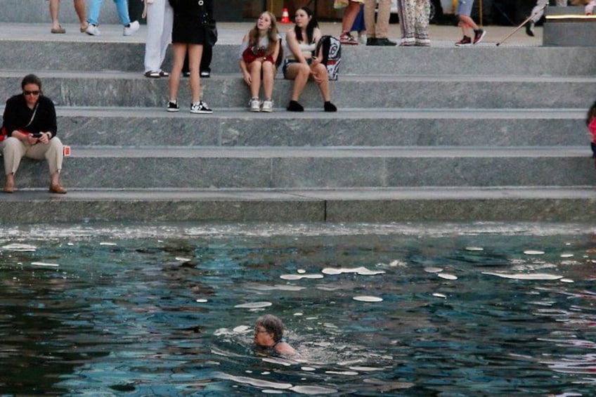 A swimming pool with people sitting on steps and a person swimming. 3
