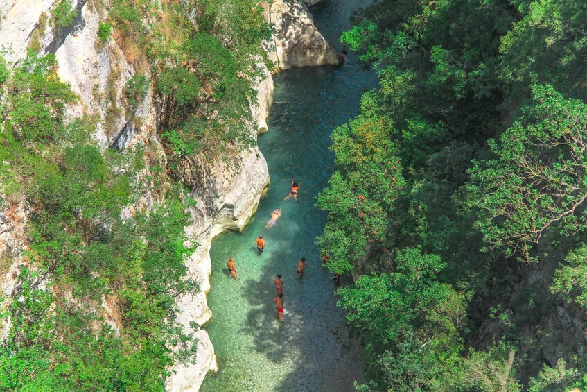 A group of people swimming in a clear river surrounded by cliffs and dense greenery. 3