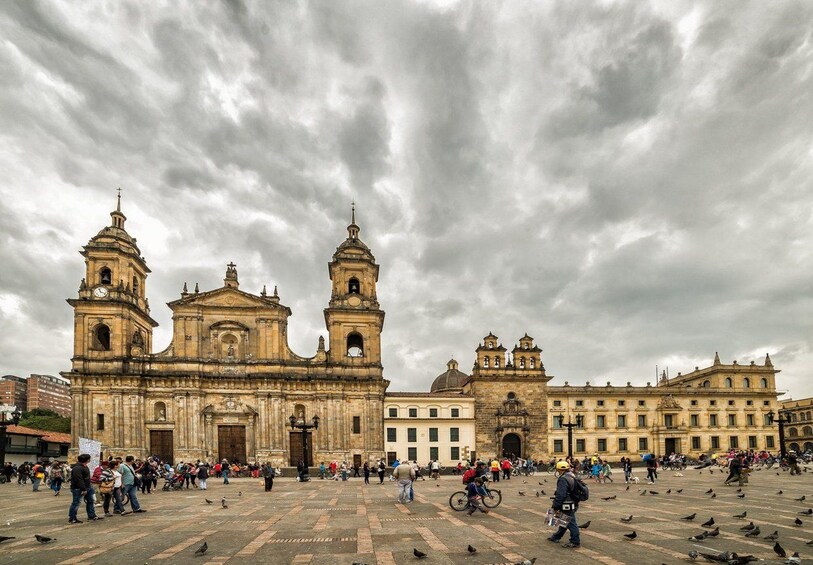 A historic plaza with a large cathedral and a smaller adjacent building, surrounded by a crowd of people and pigeons. 1