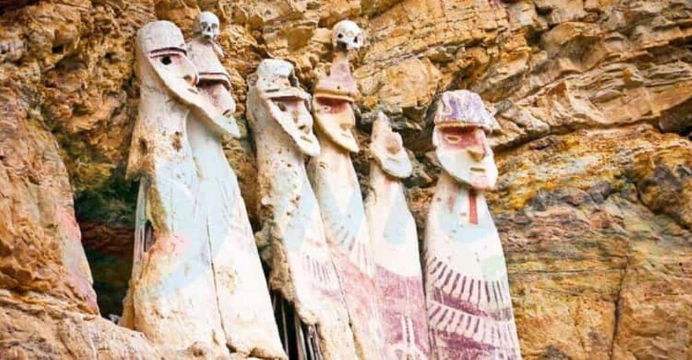Una serie de figuras de piedra tallada con rasgos faciales definidos, frente a un escarpado muro rocoso. 4