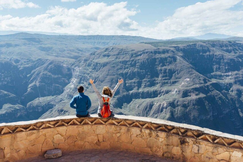 Dos personas sentadas en un muro de piedra con vistas a un paisaje montañoso. 1