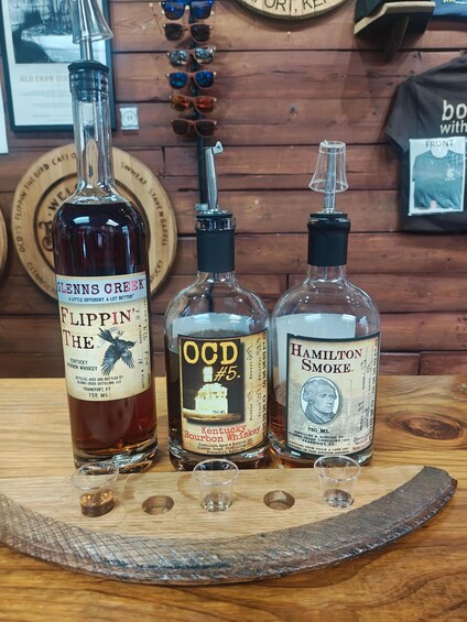 Drei Whiskey-Flaschen auf einem Holztisch mit Gläsern und einem hölzernen Hintergrund. 3