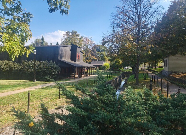 Ein rustikales Gebäude mit einer Veranda, umgeben von üppigem Grün und einem kleinen Bach. 2