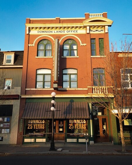 A brick building with a sign reading 'Dominion Lands Office' and 'Tunnel 25 Years' on the storefront. 4