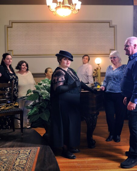 A group of people in a room with a chandelier, a piano, and a large plant. 3