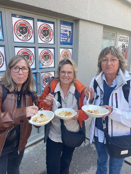 Three people holding plates of food in front of a building with multiple signs for Taekwondo Klub Pantera Zagreb. 5