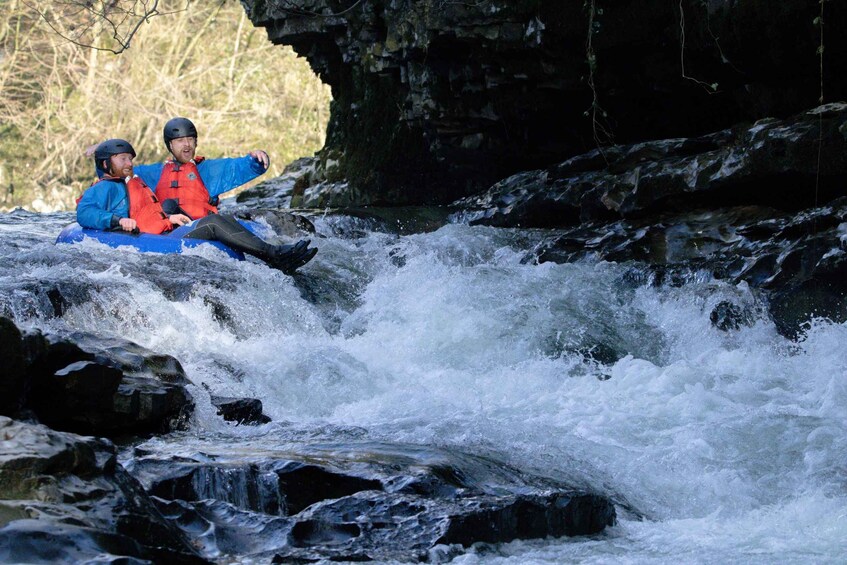Two people in a blue raft navigating a river with rapids. 4