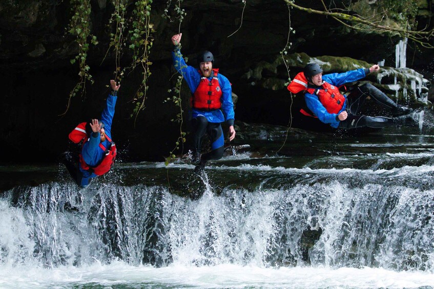 Three people jumping off a waterfall in blue jackets and red life vests. 2