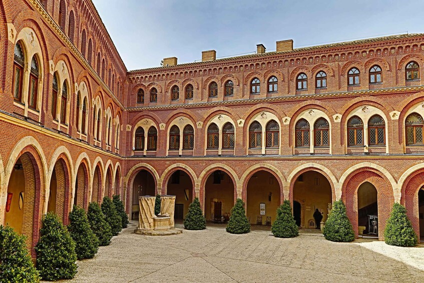 A courtyard with red brick buildings, arched windows, and a central fountain. 5